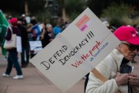 A photo of a woman holding a sign at a protest that reads, "Defend democracy; We the people... U.S. Constitution."