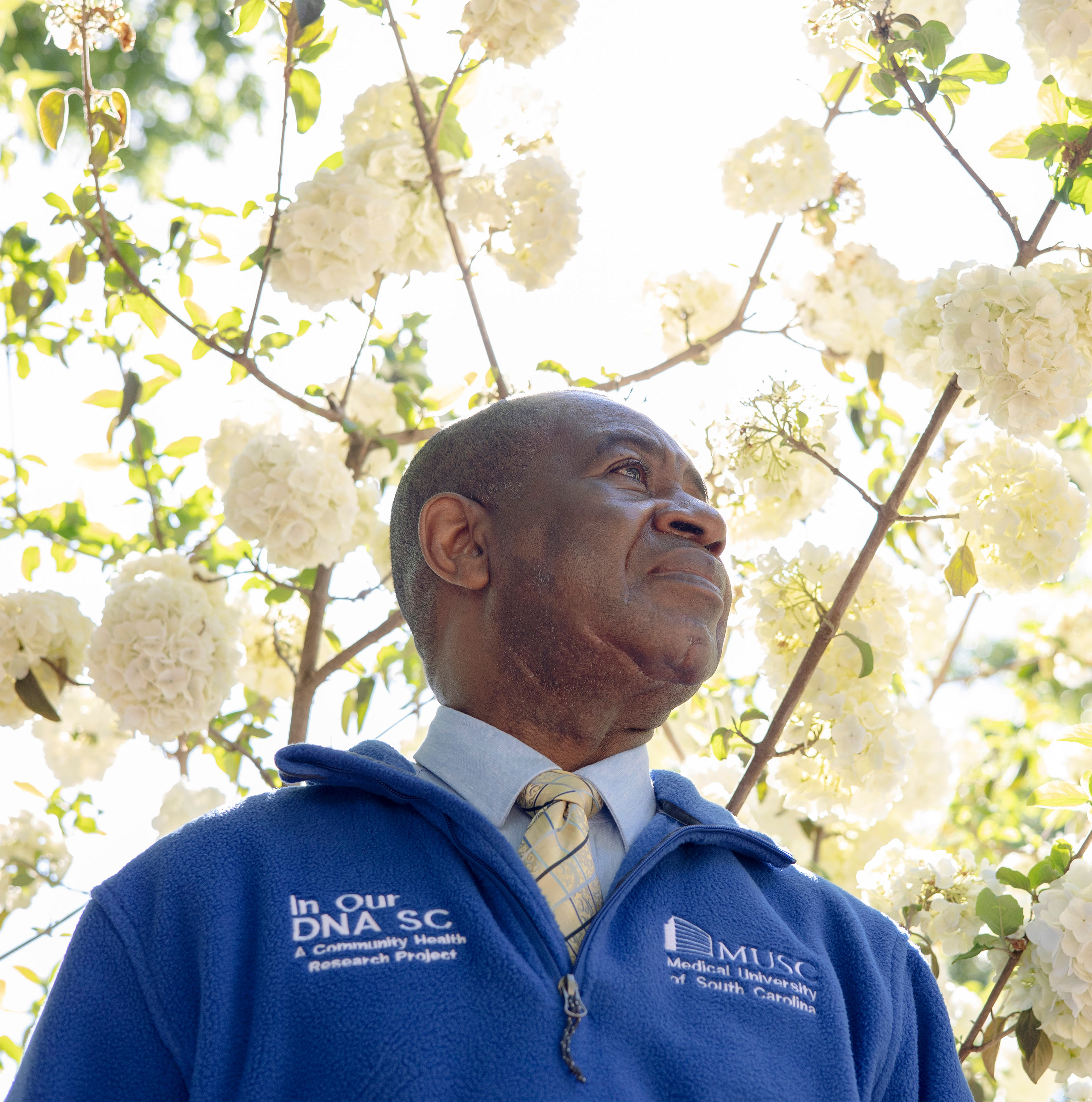 A photo of Lee Moultrie outside. The portrait is shot from below, so his head is framed by white blooms on the trees above him.