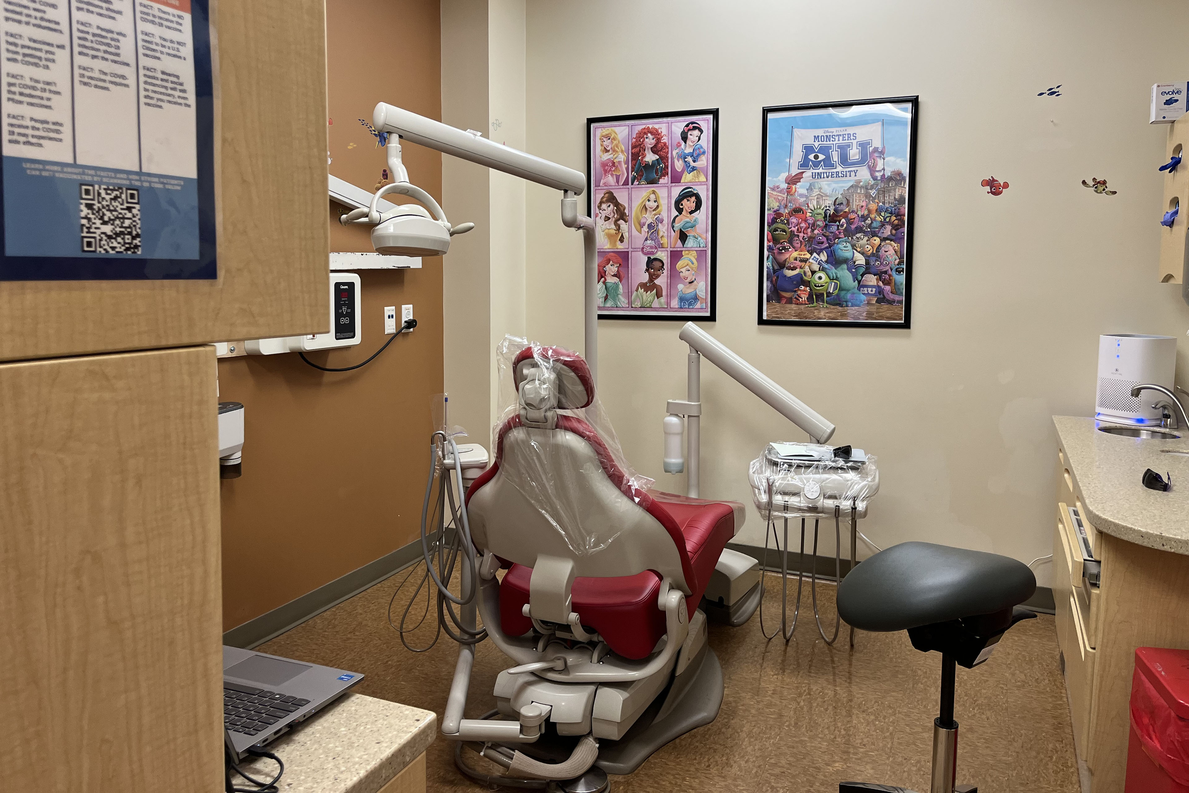 An empty dental exam room. It has a red chair and Disney movie posters on the wall.