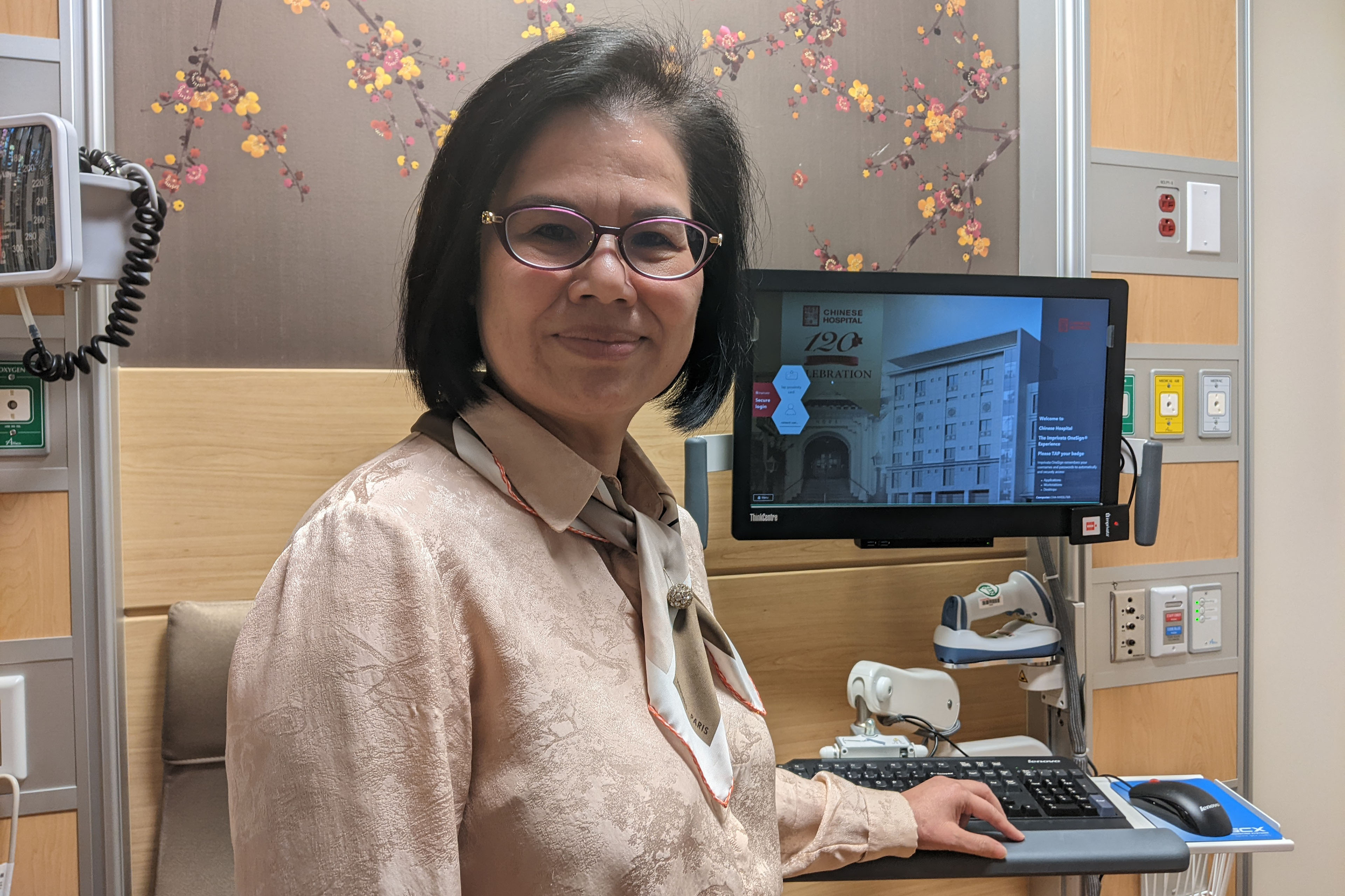 Jian Zhang stands beside an intake computer in a doctor's office.