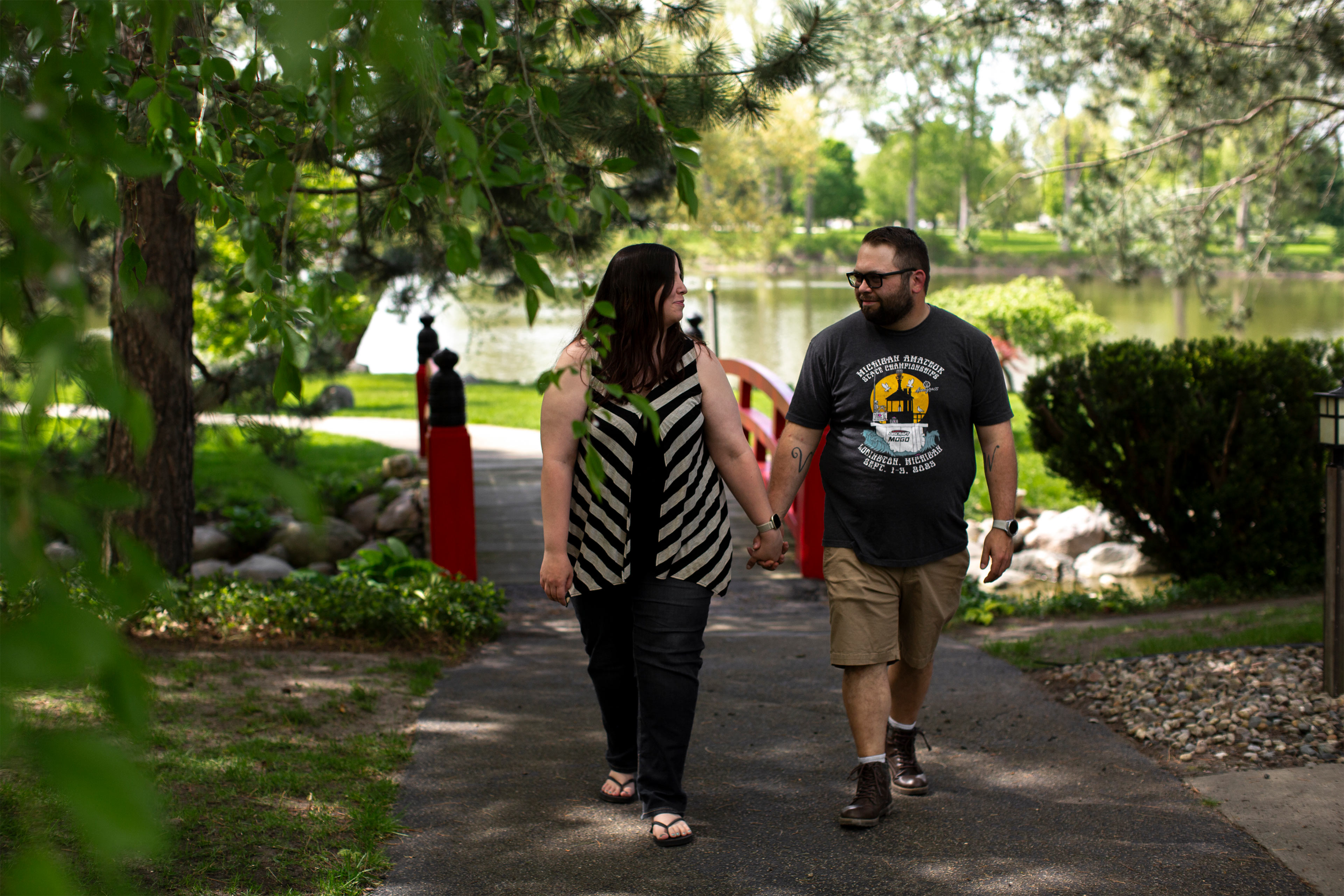 A man and a woman hold hands and look at each other while walking on a path in a park.