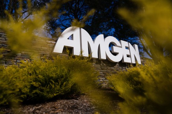 A photo of the Amgen logo sign outside of its headquarters, framed by foliage.