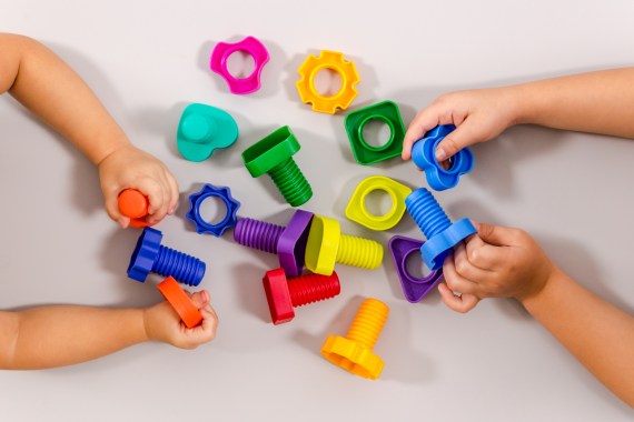 Two children play with colorful screw-like toys, only their hands are visible