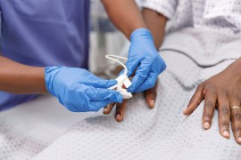A close-up photo of a medical professional placing a pulse oximeter on the finger of a hospitalized patient who is lying in bed.