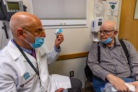 A photo of a doctor holding up a dry powder inhaler to show his patient sitting next to him.