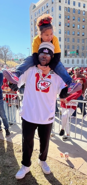 A photo of a man at the Kansas City Chiefs Super Bowl parade carrying his daughter on his shoulders.