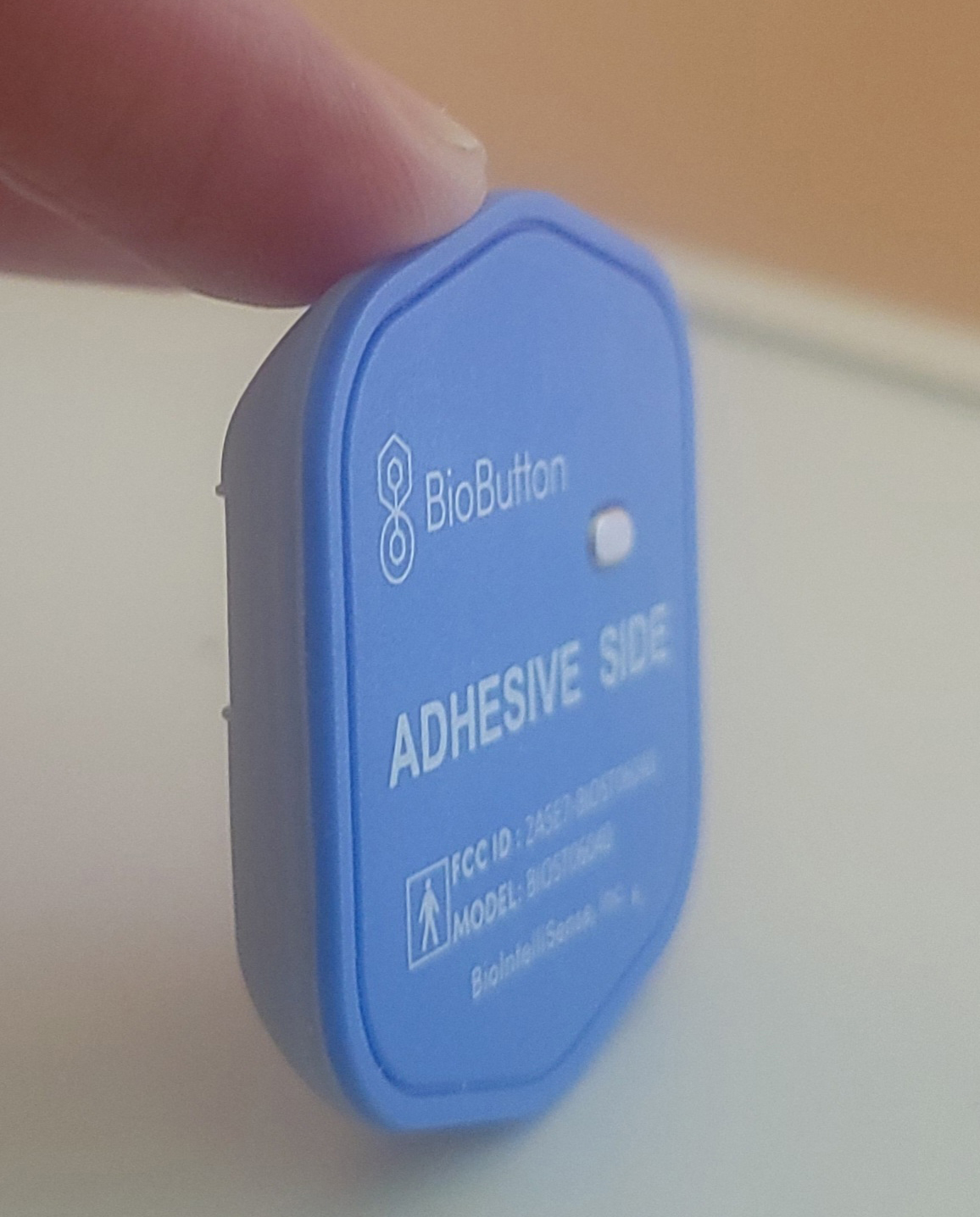 A photo of a BioButton being held up by a finger.