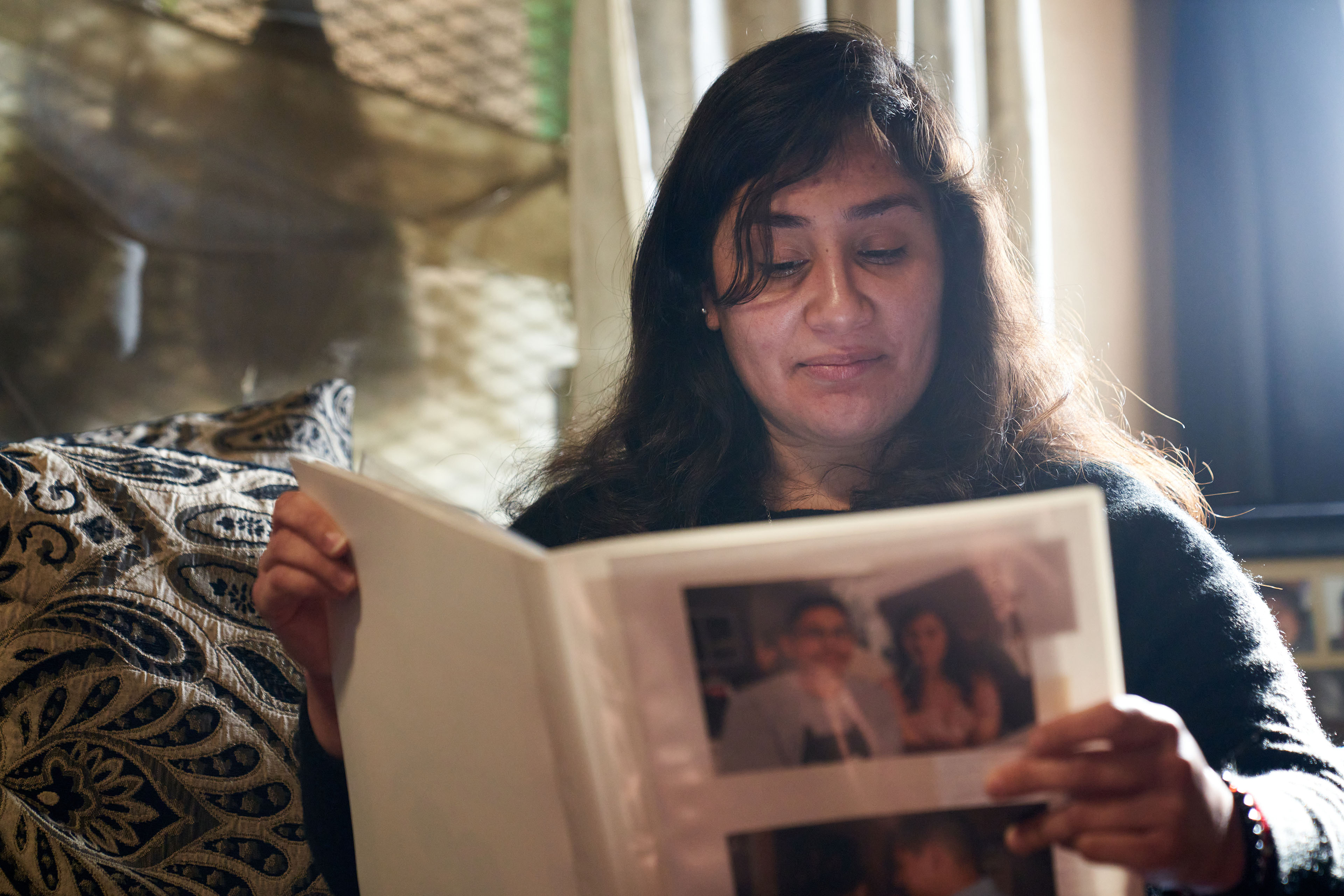 A portrait of María Rivas Cruz, looking through a scrapbook in her home.