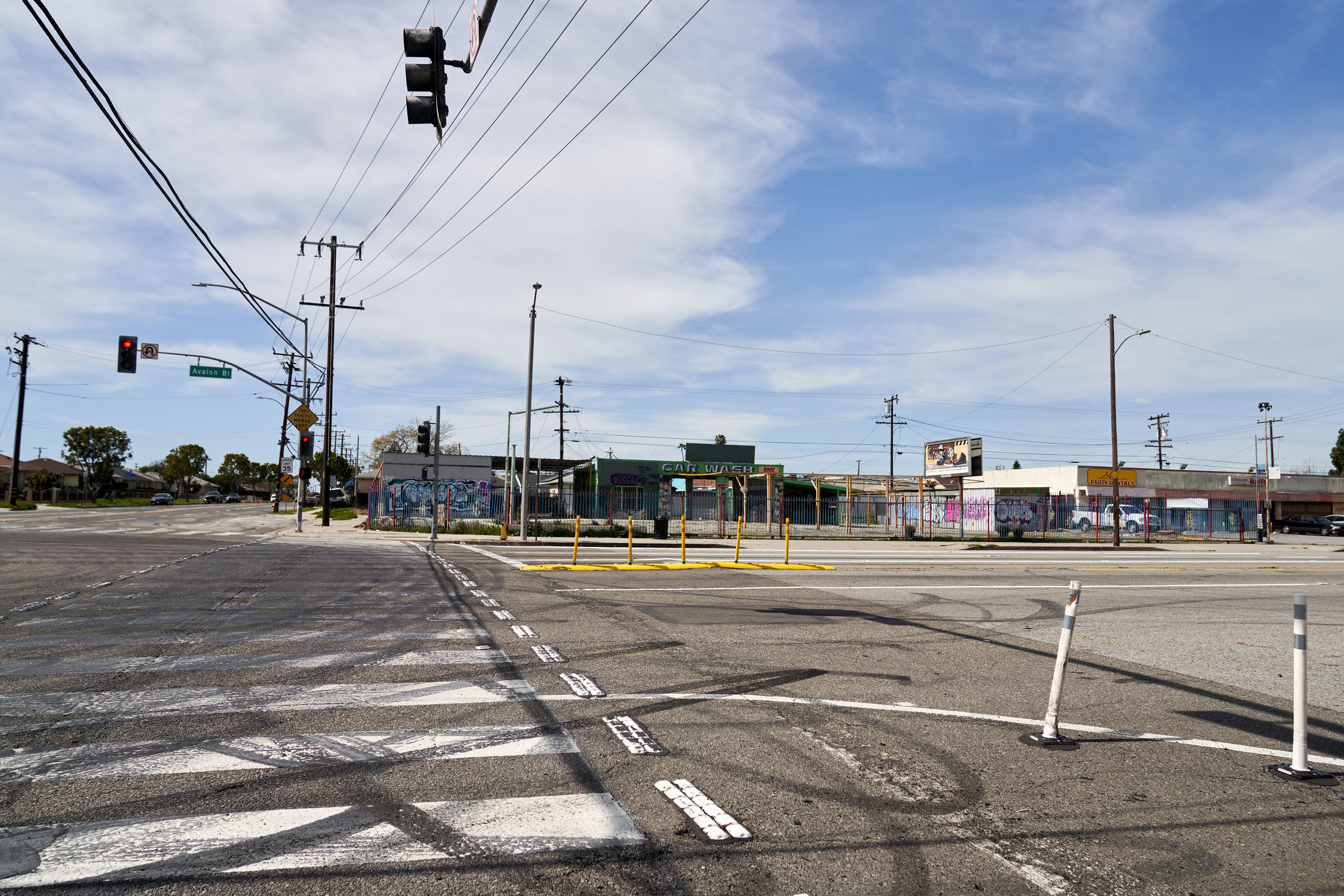 A photograph shows a large intersection. There is a crosswalk, but the painted lines are badly faded. Dark tire marks are visible on the pavement.