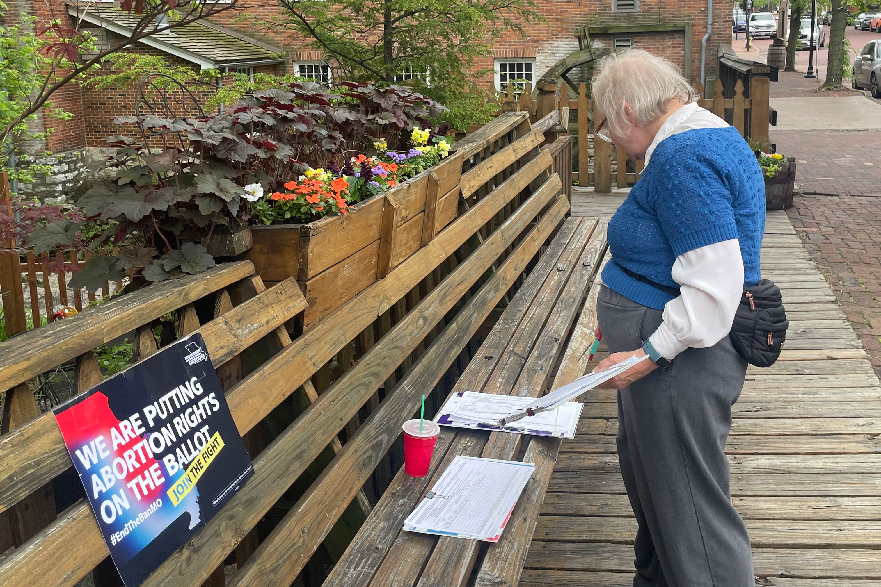 Image of a woman looking at a bench with papers and a sign that reads, "We're putting abortion rights on the ballot. Join the fight."