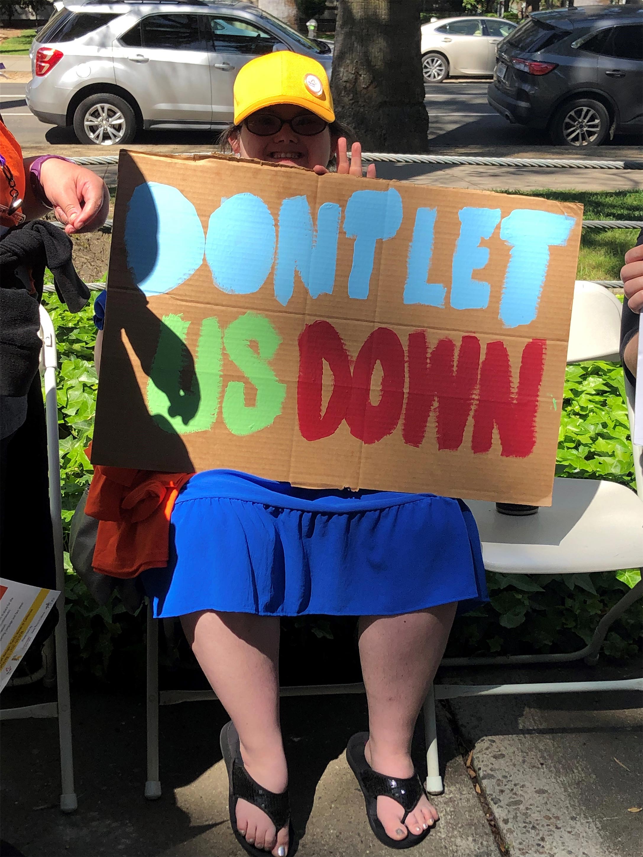 A photo of an demonstrator sitting and holding a sign that reads, "Don't let us down."
