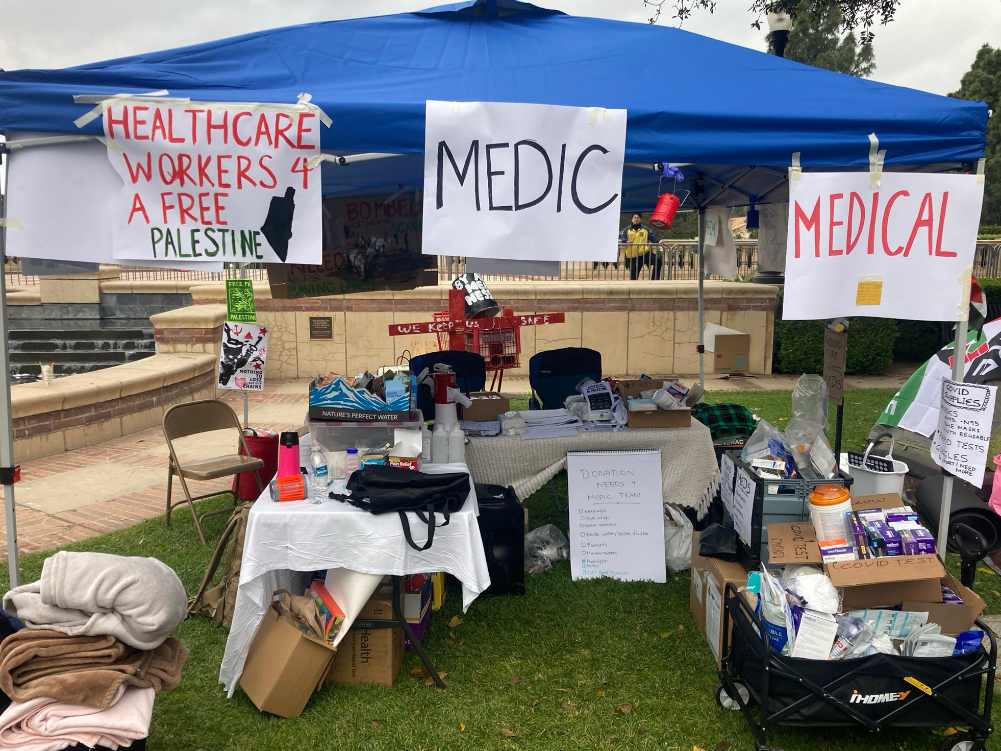 Uma foto de uma tenda médica improvisada com cartazes que diziam: "Profissionais de saúde por uma Palestina livre," junto com placas que a identificam como uma tenda médica.
