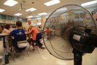 A photo of a fan setup in a classroom as a teacher helps students with their work.