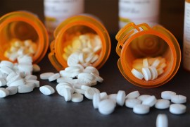 A photo of three prescription bottles with white pills spilling out of them.