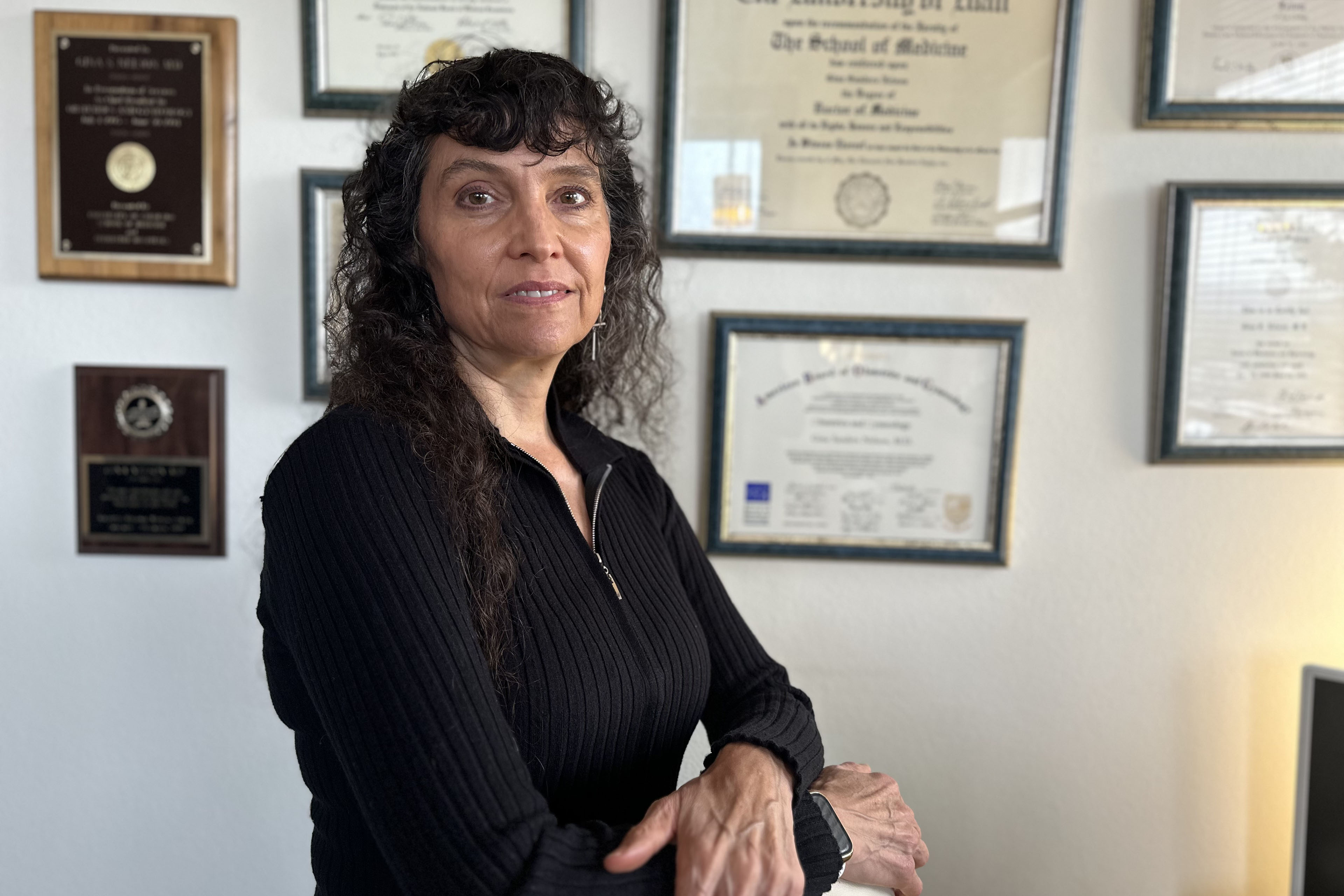A portrait of Gina Nelson standing in her office. Certificates hang on the wall behind her.