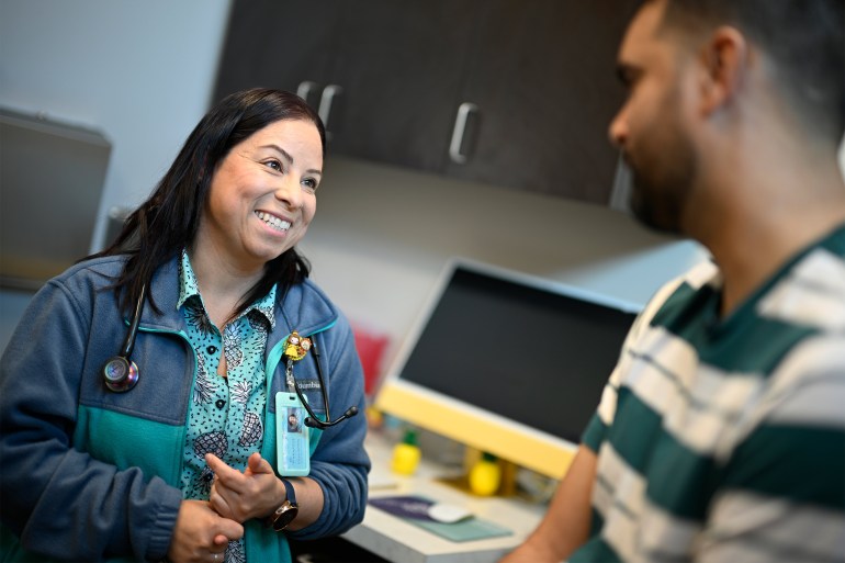 A photo of a female nurse practioner smiling while speaking to a patient.