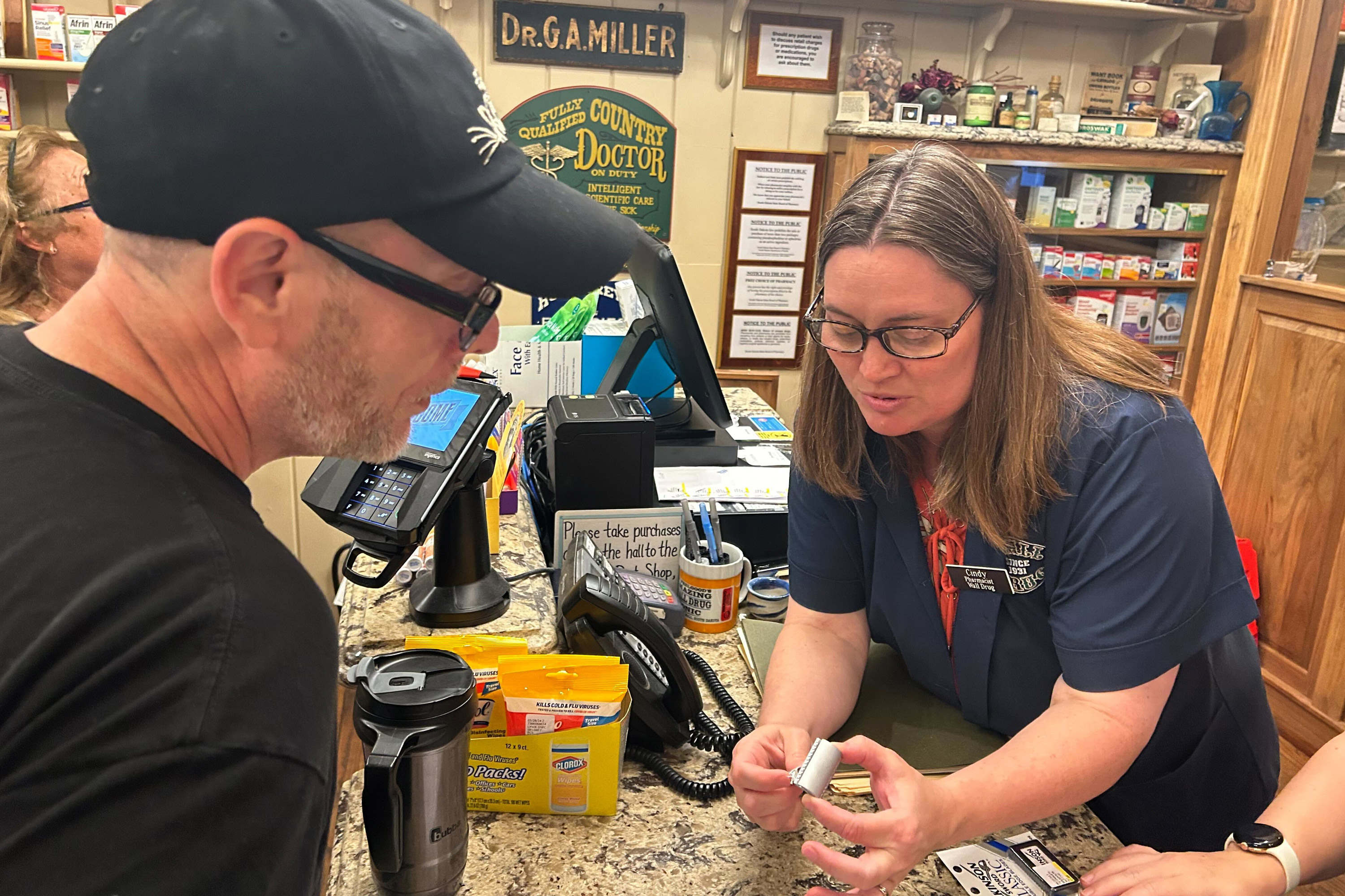 A photo of a pharmacist scanning a tourist's items at a cash register.