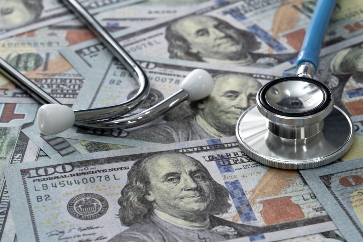 A stethoscope atop hundred-dollar bills on a flat surface.