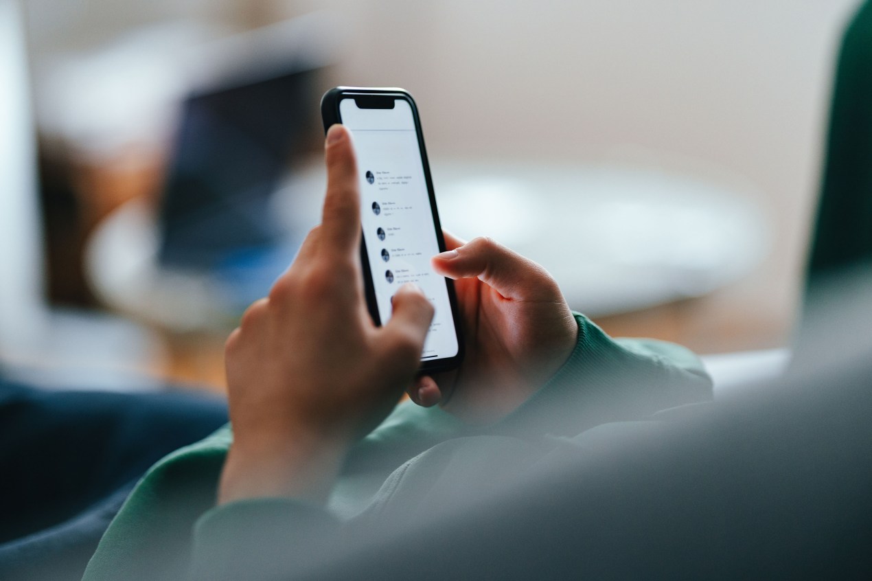 An unrecognizable teen is checking social media notifications on their smartphone while lying on a couch at home.