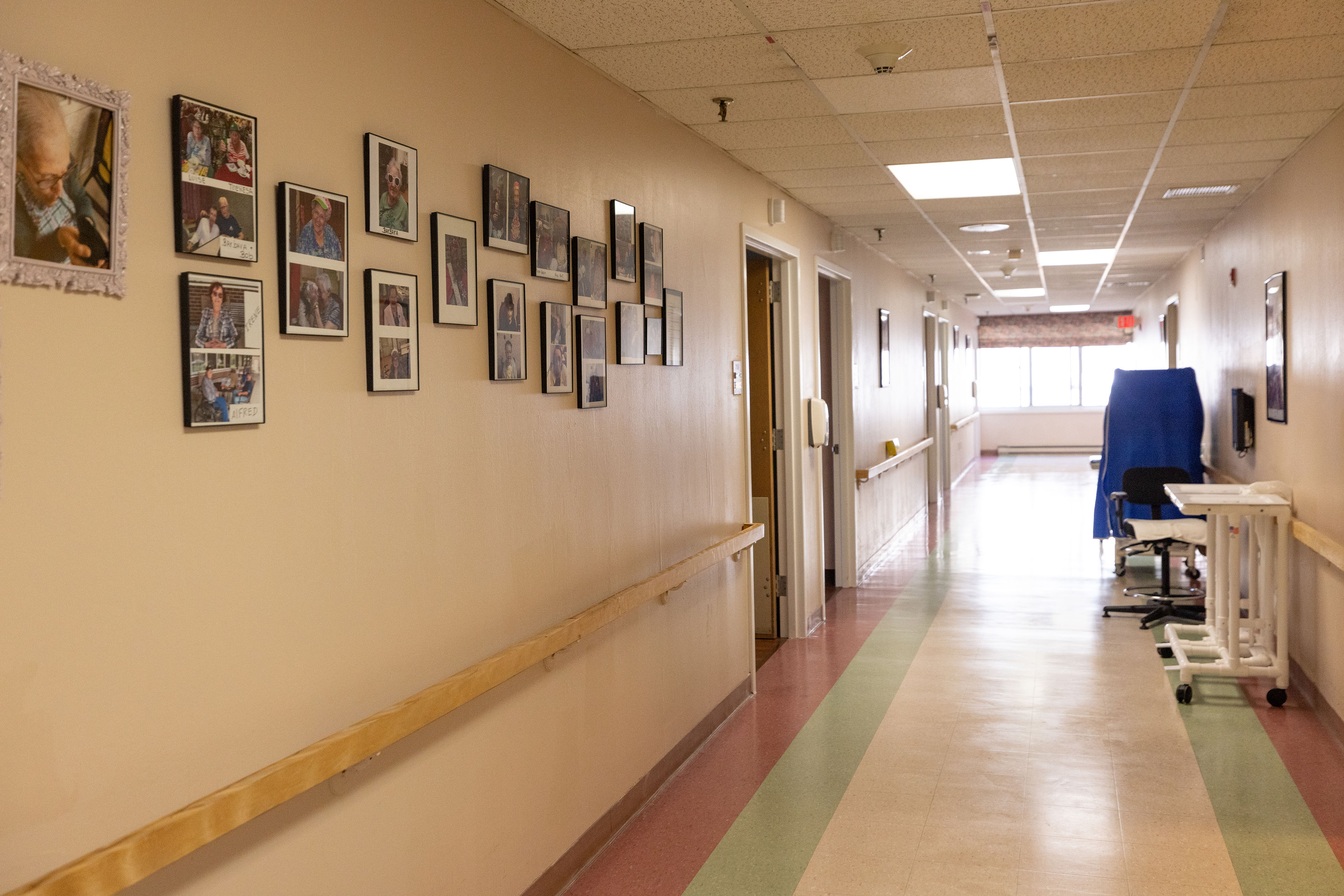 A hallway of a nursing home with family pictures on the wall and bright windows at the end of the hallway