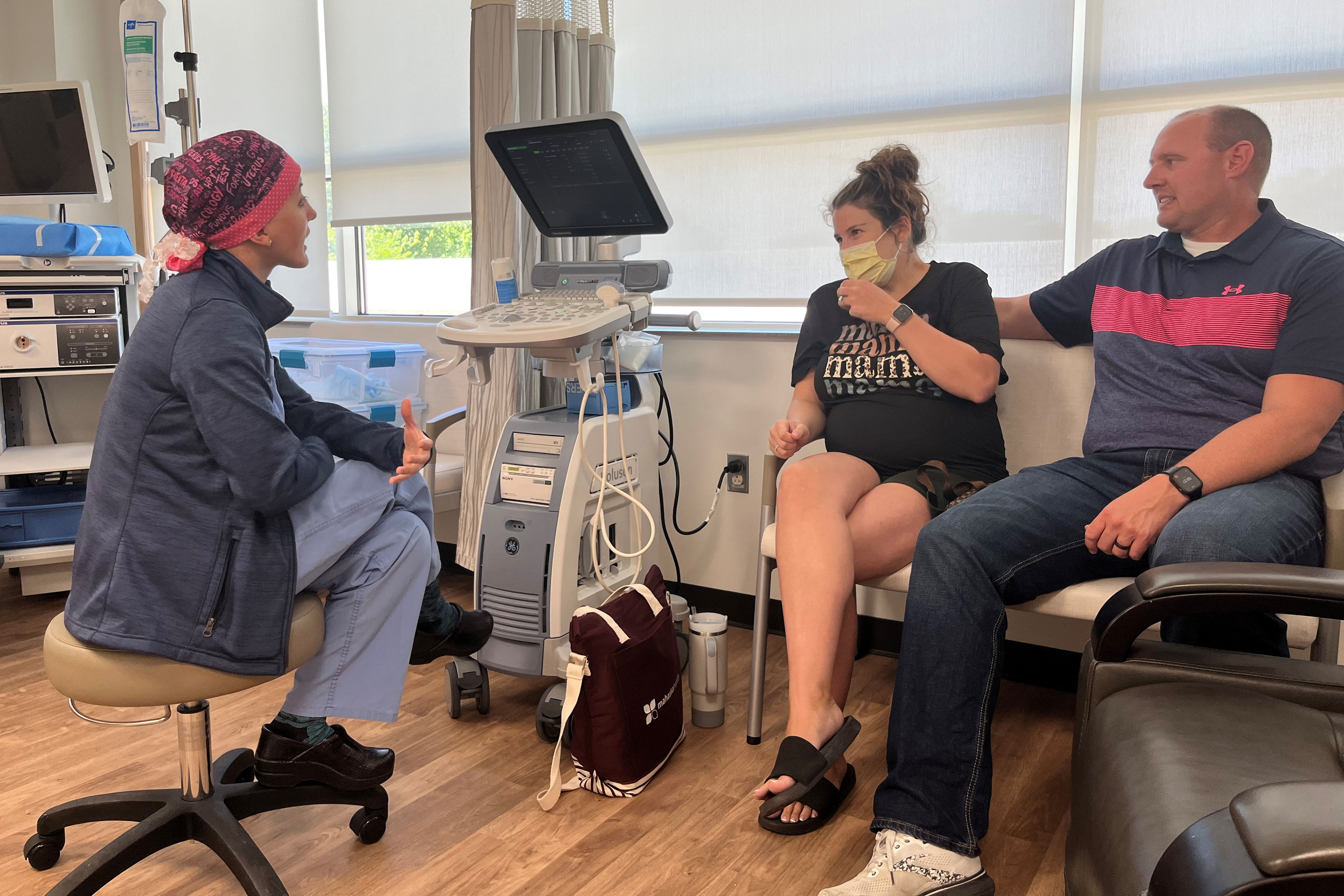 Obstetrician Taylar Swartz speaks with patient Addie Comegys and her husband, Jeff Comegys in an exam room.