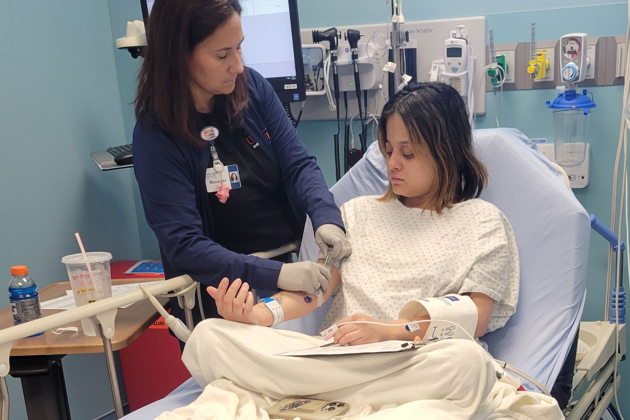 A female nurse treats a female patient who is sitting in a hospital bed.