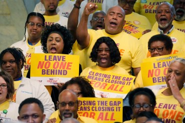 A photo of a group of activists holding signs that read, "Leave no one behind," and "Closing the coverage gap means closing it for all."