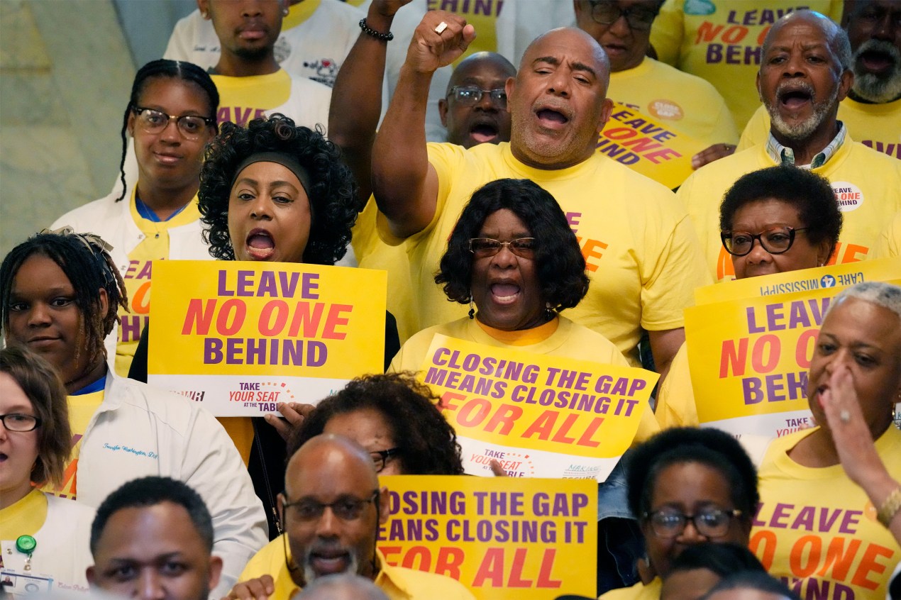 A photo of a group of activists holding signs that read, "Leave no one behind," and "Closing the coverage gap means closing it for all."