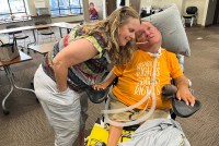 A woman leans down to put her face close to a man in an electronic wheelchair.