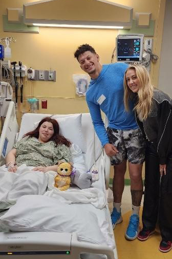 A photo of a girl in a hospital bed with two adults standing beside the bed.