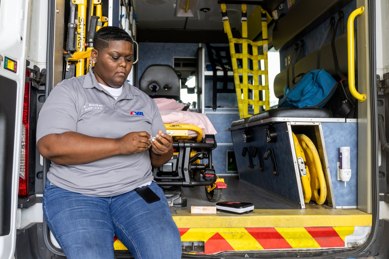 A photo of a woman leaning on an ambulance while holding naloxone.