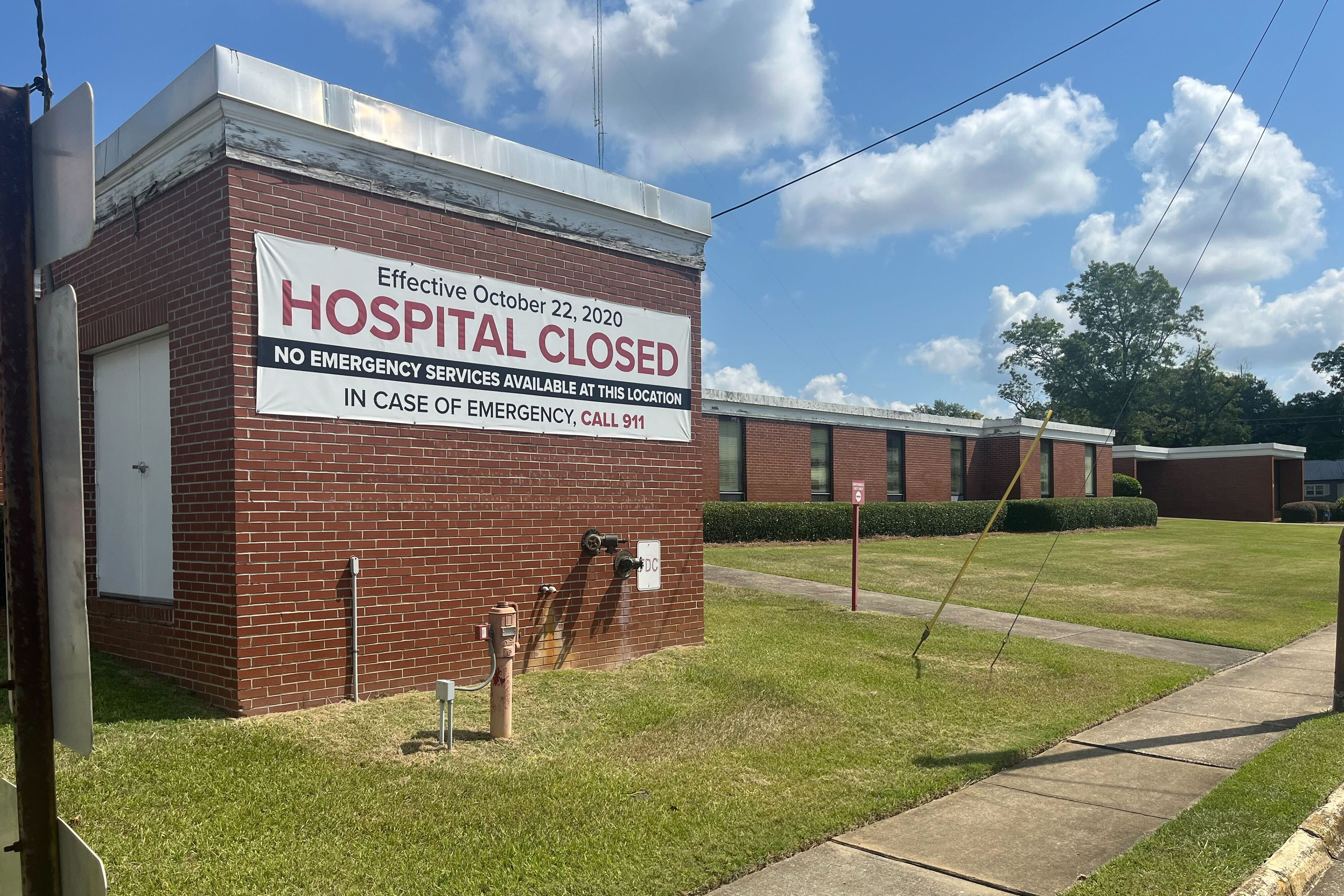 An exterior photograph of a hospital building made of brick. It has a large sign on the side that says, "Effective October 22, 2022 / HOSPITAL CLOSED / No emergency services available at this location / In case of emergency, call 911."