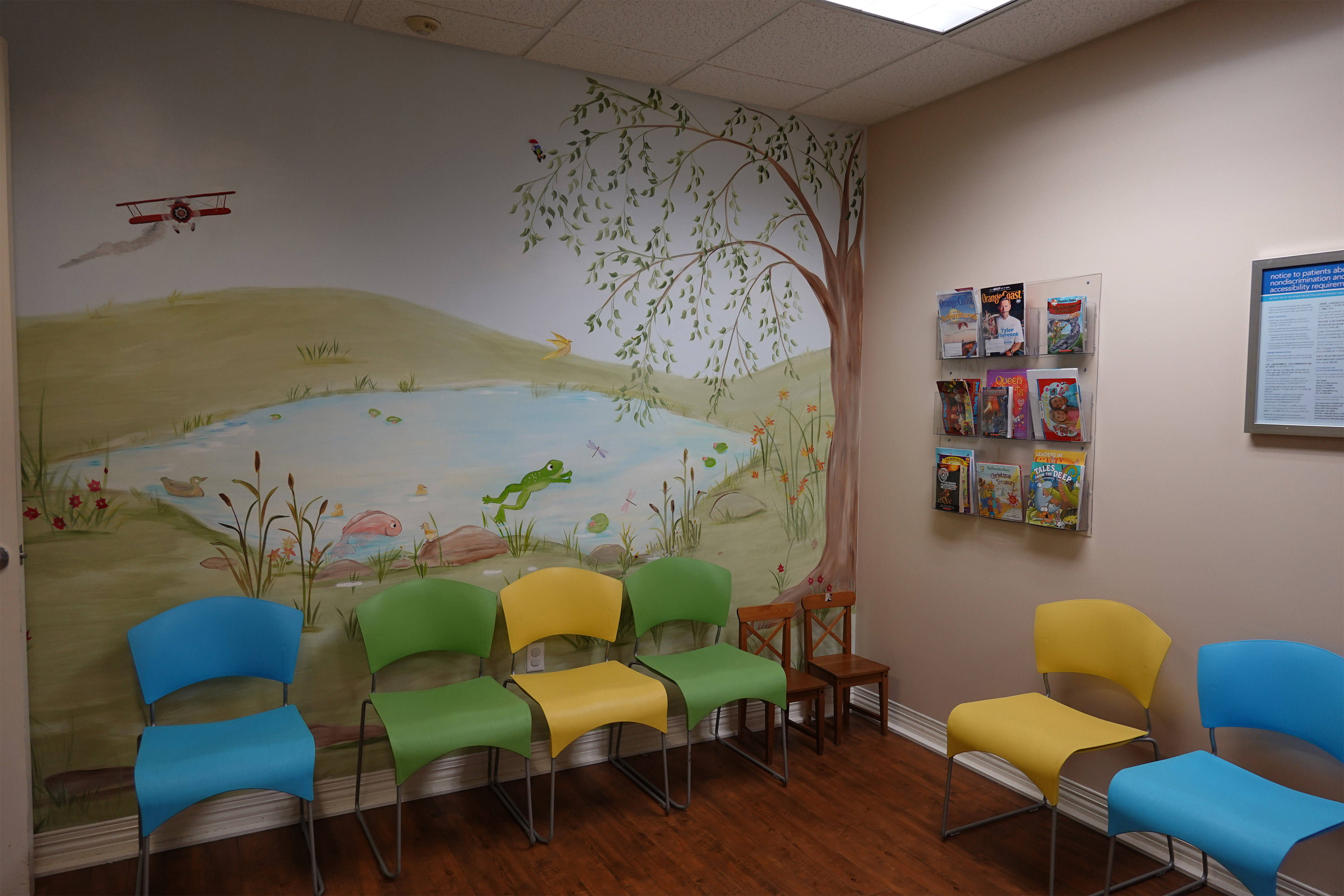 A photo of a pediatrician's waiting room with murals and colorful chairs.