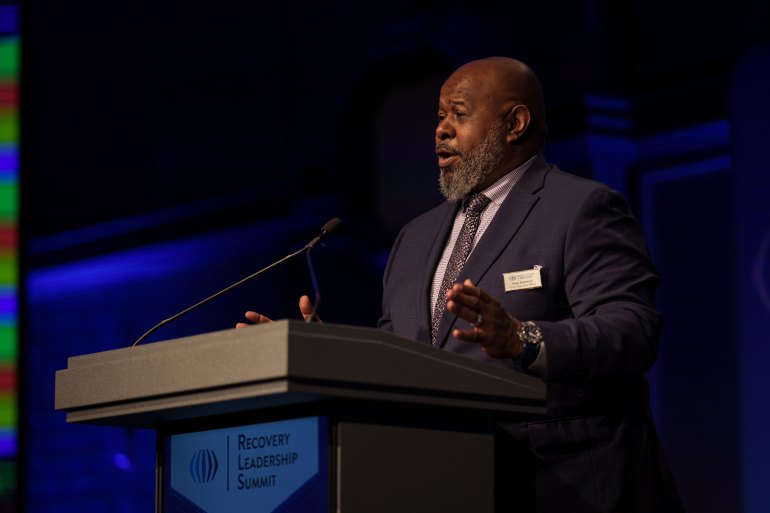 A man speaks into a microphone mounted on a lectern.