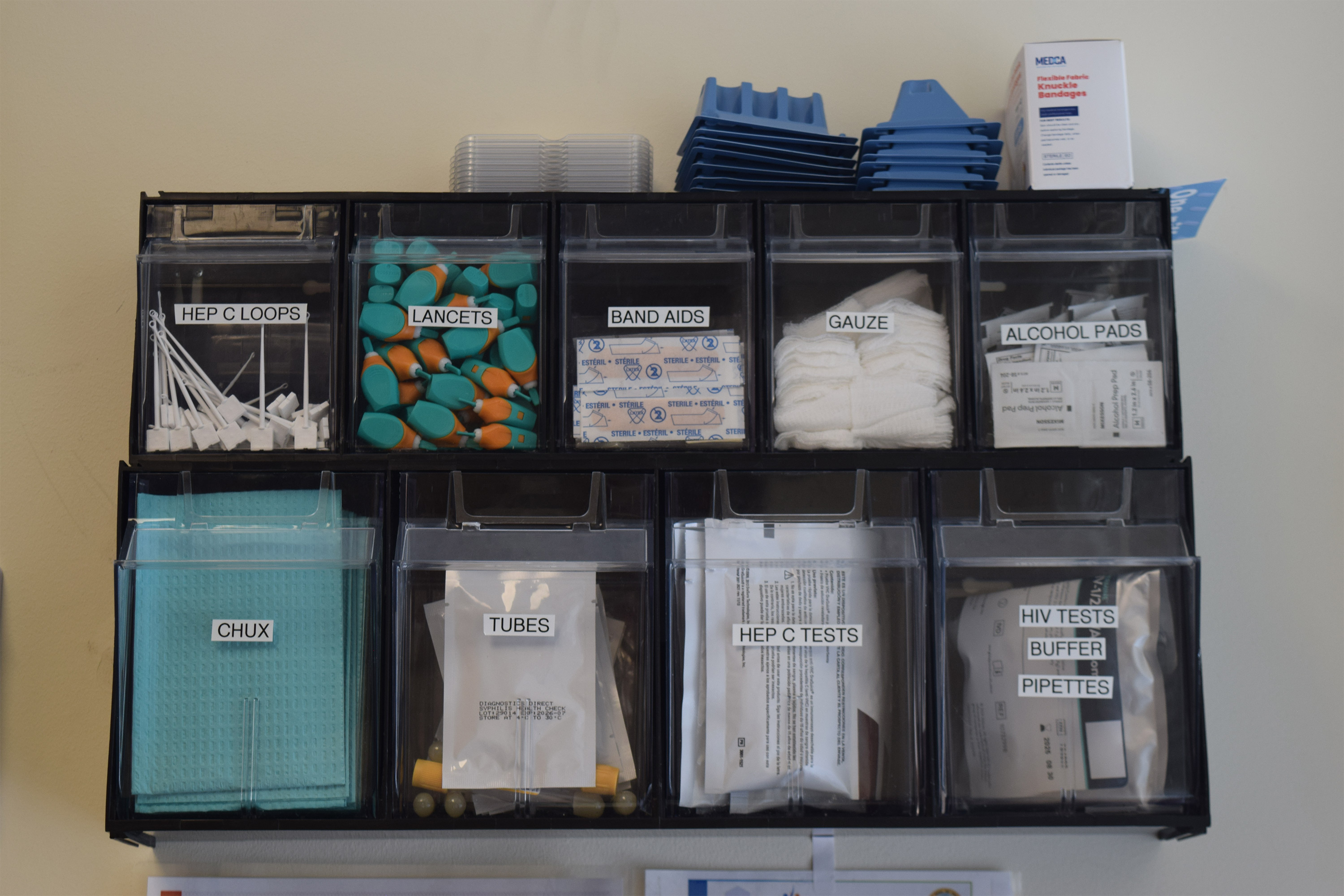 A photo of a shelf filled with alcohol pads, lancets, HIV tests, and hepatitis C tests.