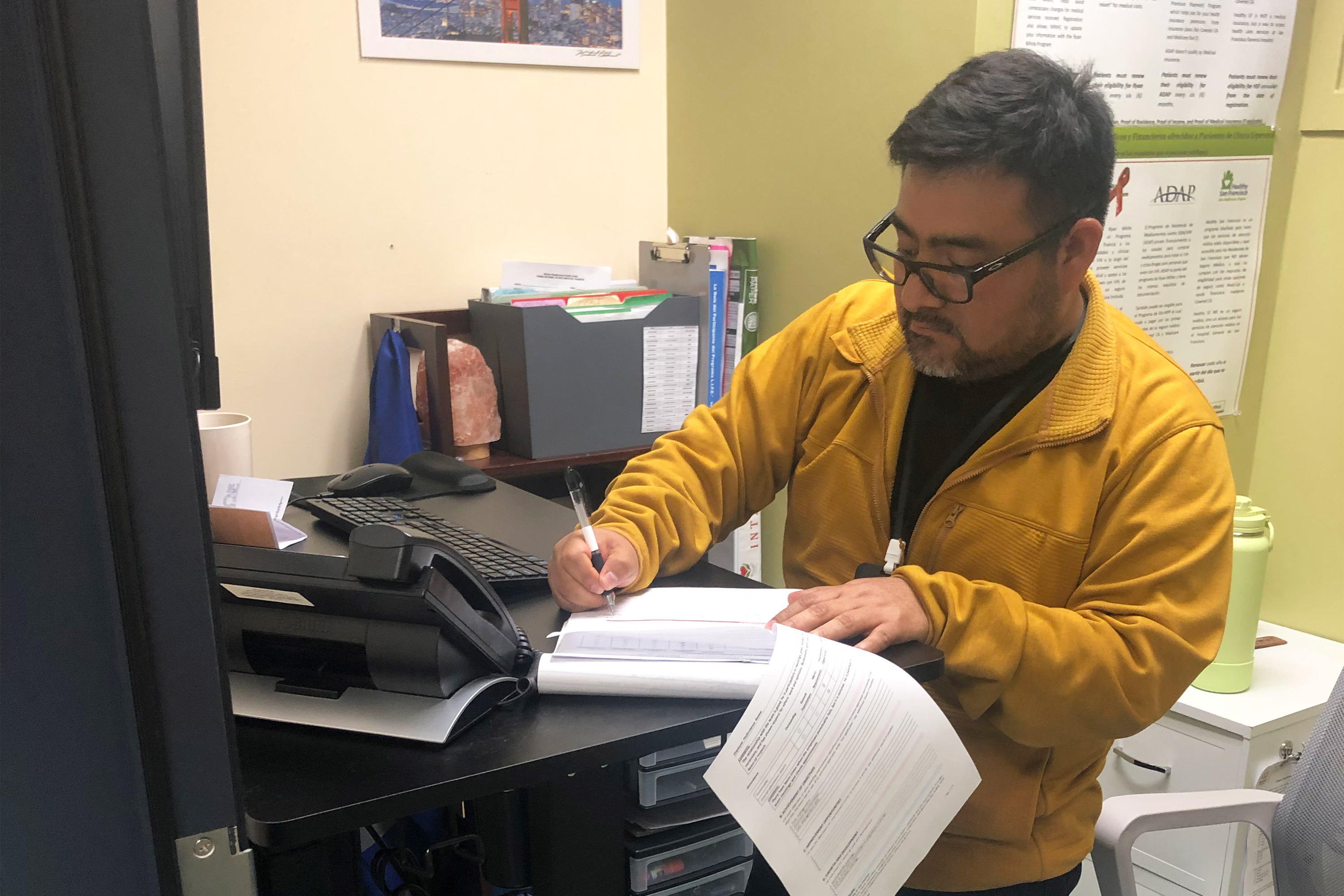 Retrato de un hombre de pie junto a un escritorio, sosteniendo papeles.