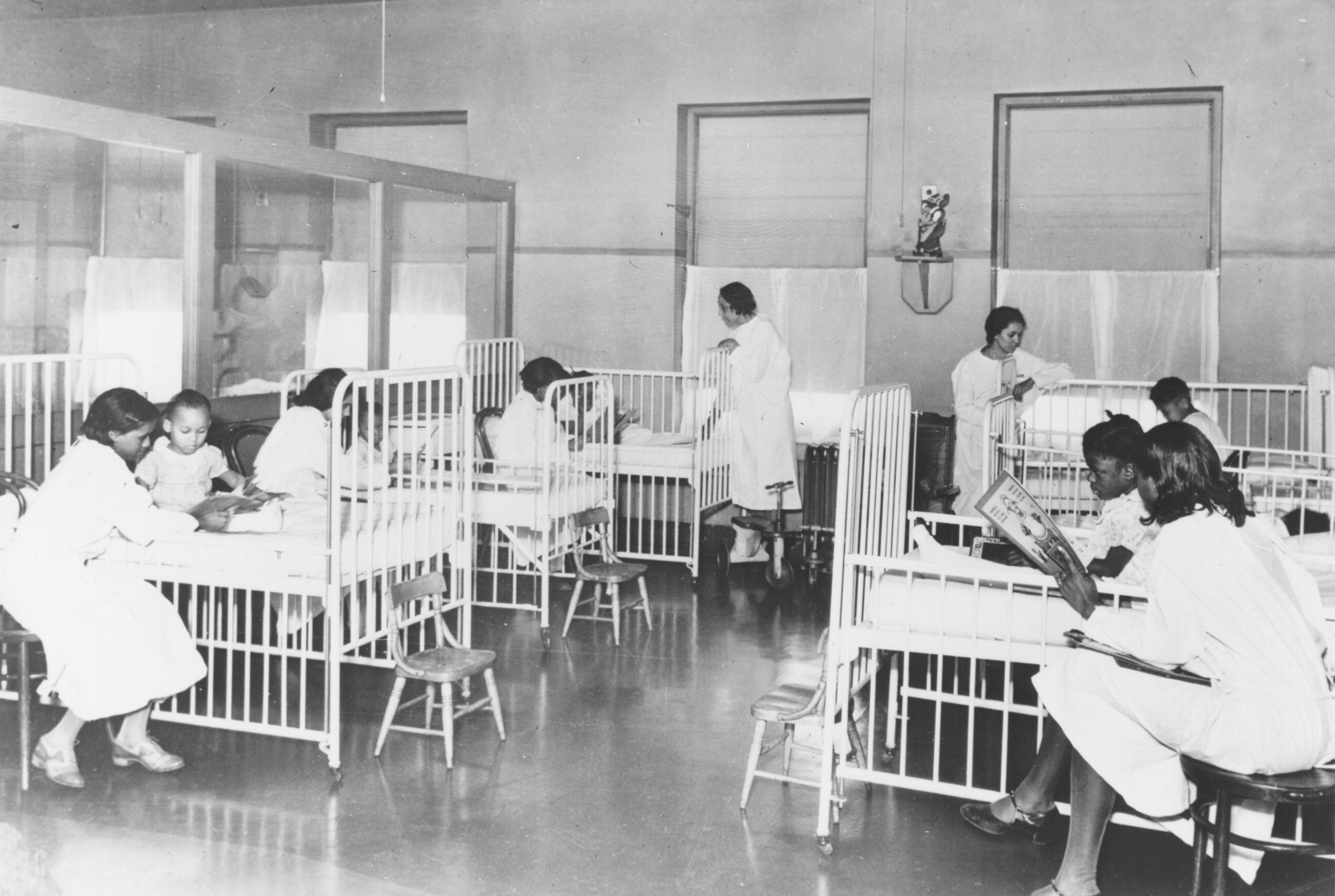 An archival photo of a Black hospital with nurses attending to child patients.