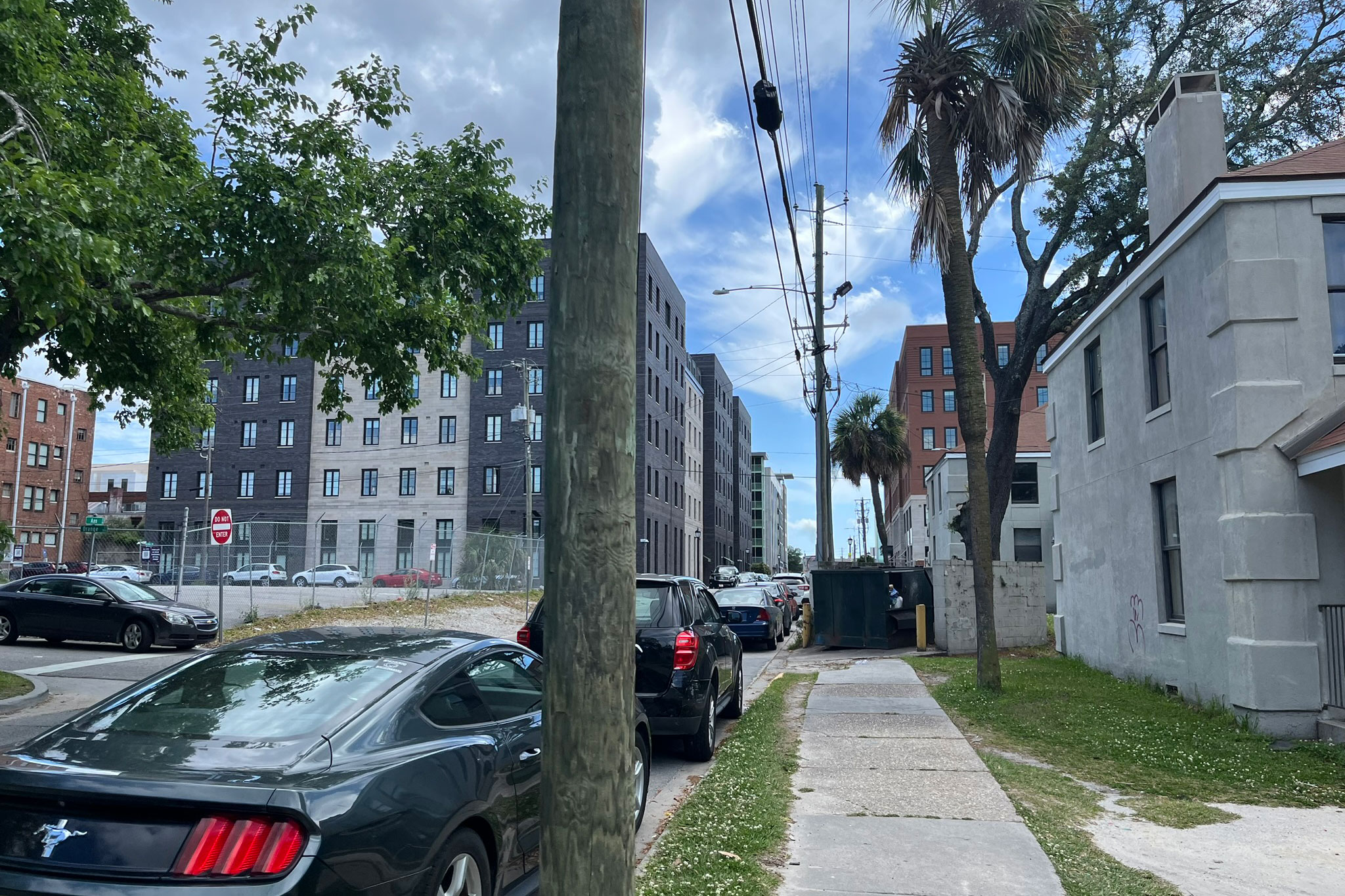 A view down a narrow street where cars are parked. To the right is one of the Yamacraw Village buildings. To the left and a block in the distance is a new apartment building.