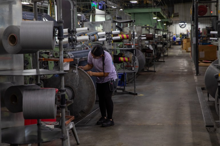 A woman in a purple t-shirt undertakes a task in a factory