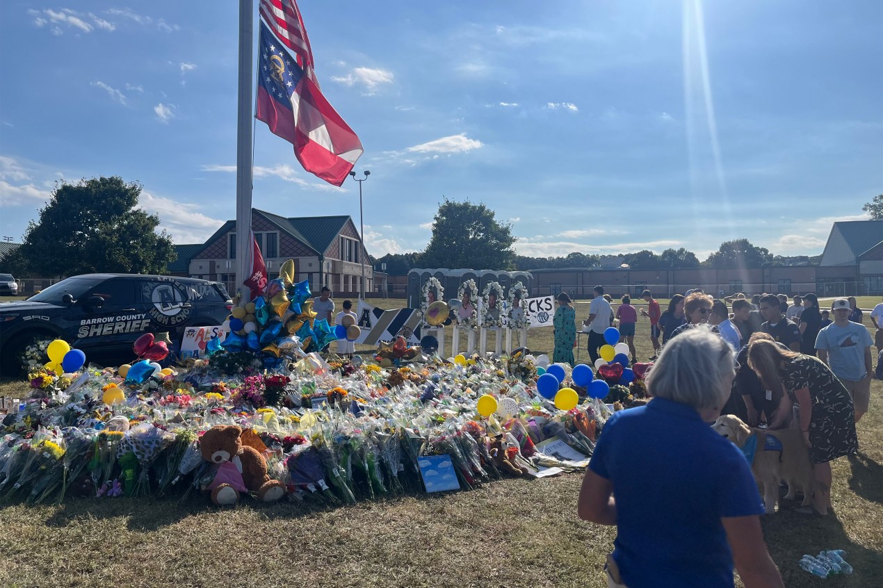 A photo of a flagpole surrounded by bouquets and stuffed animals outside of a school.