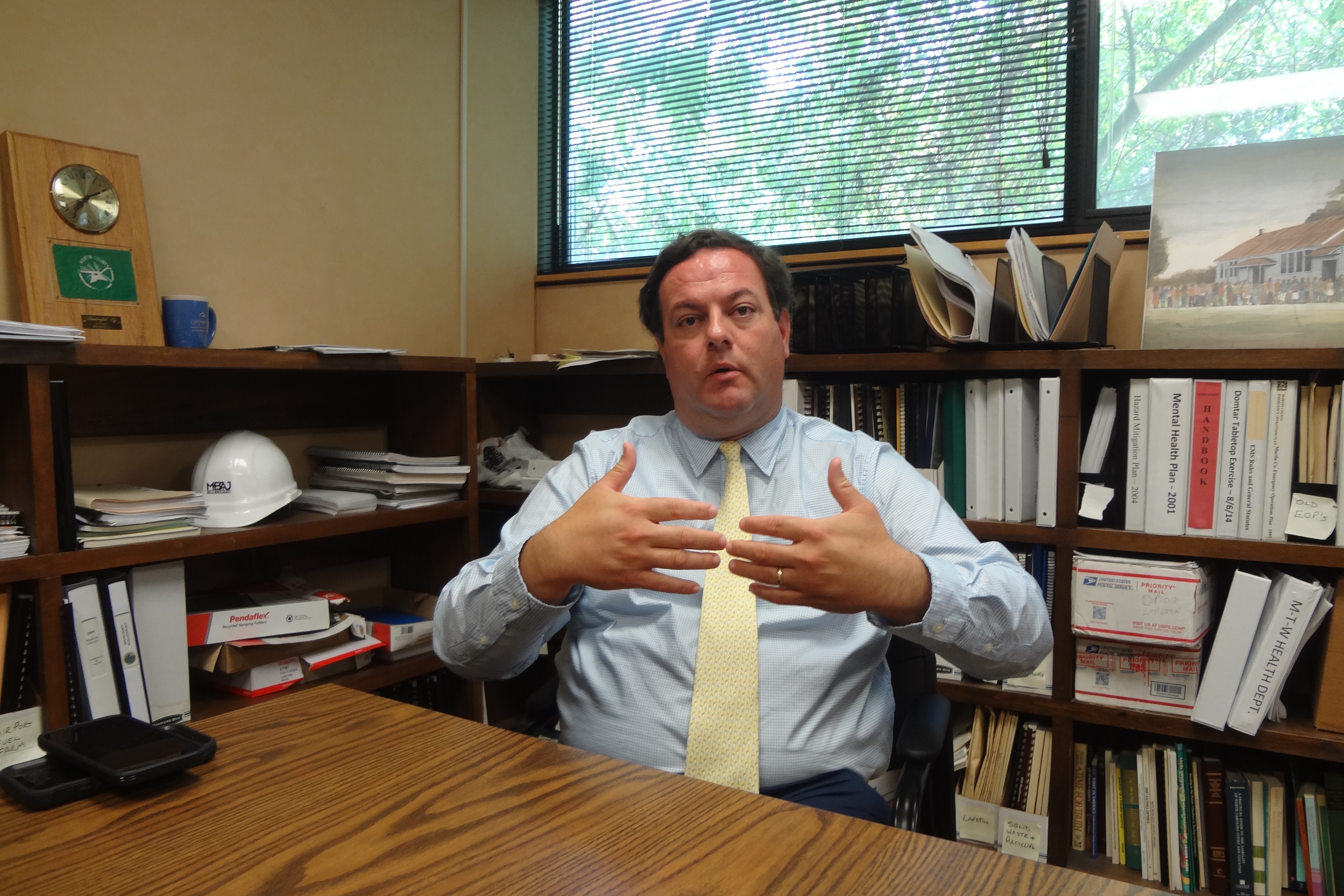 A man in a suit shirt and a yellow tie sits at a desk in an office