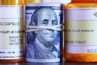 A roll of one hundred dollar bills sits among a row of prescription medication bottles.