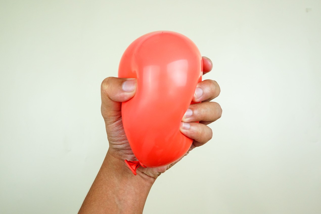 A hand tightly squeezes a small red balloon.