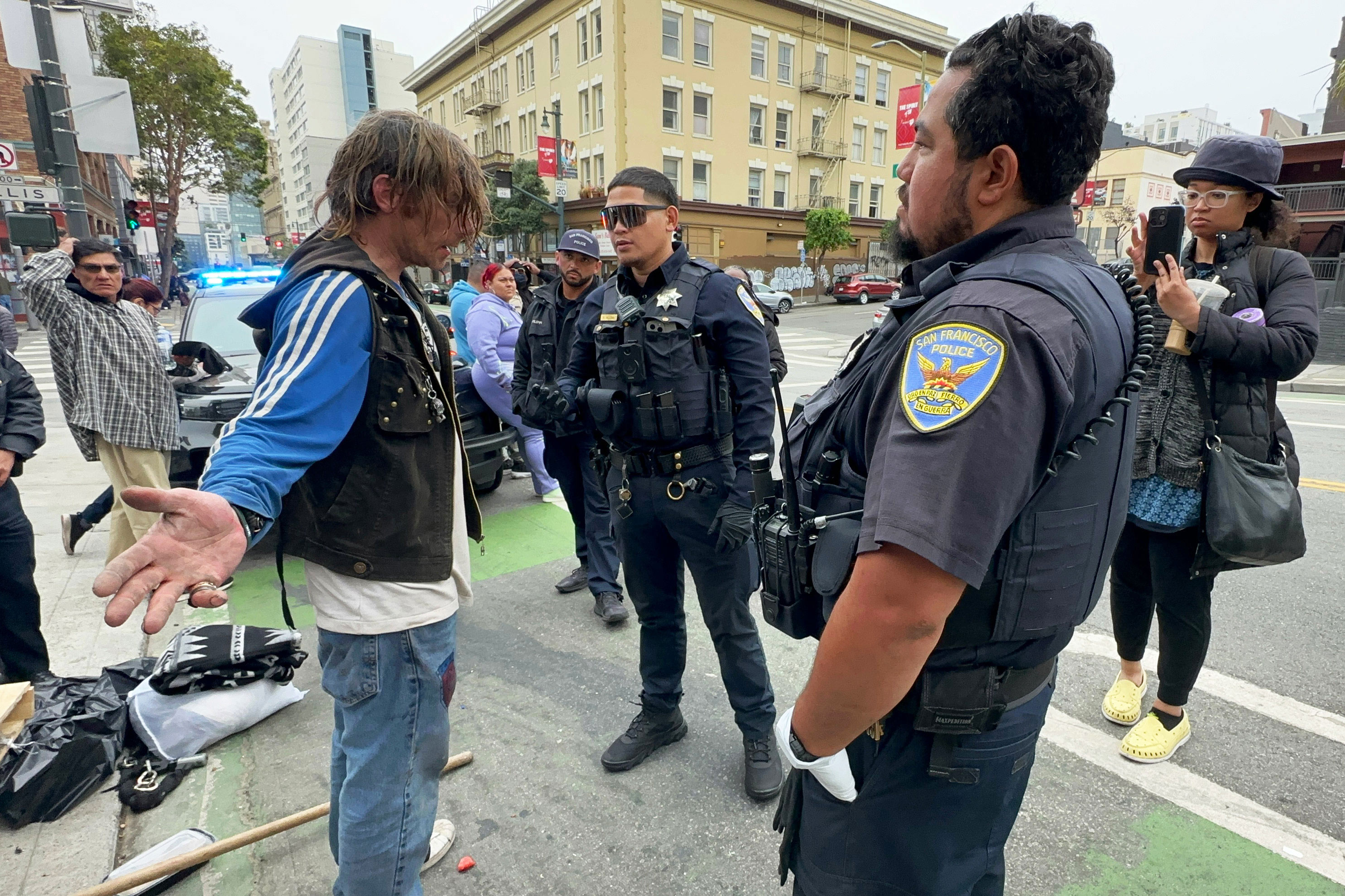 Health and Medical news A photo of Andrew Douglass with his arms fanned out, speaking to police officers.