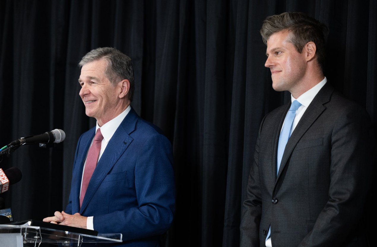 Two men in suits speak on a stage.