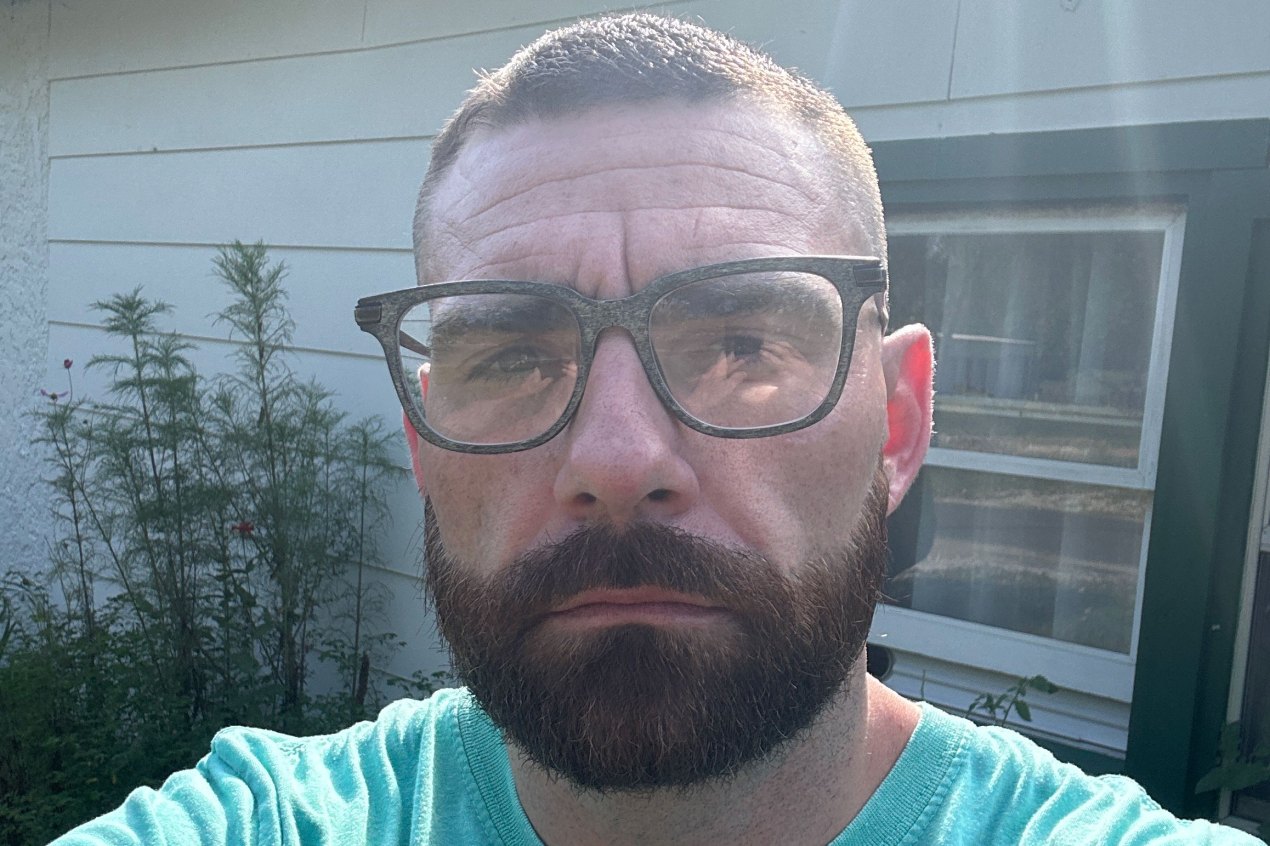 A man with a beard and glasses looks serious as he takes a selfie.