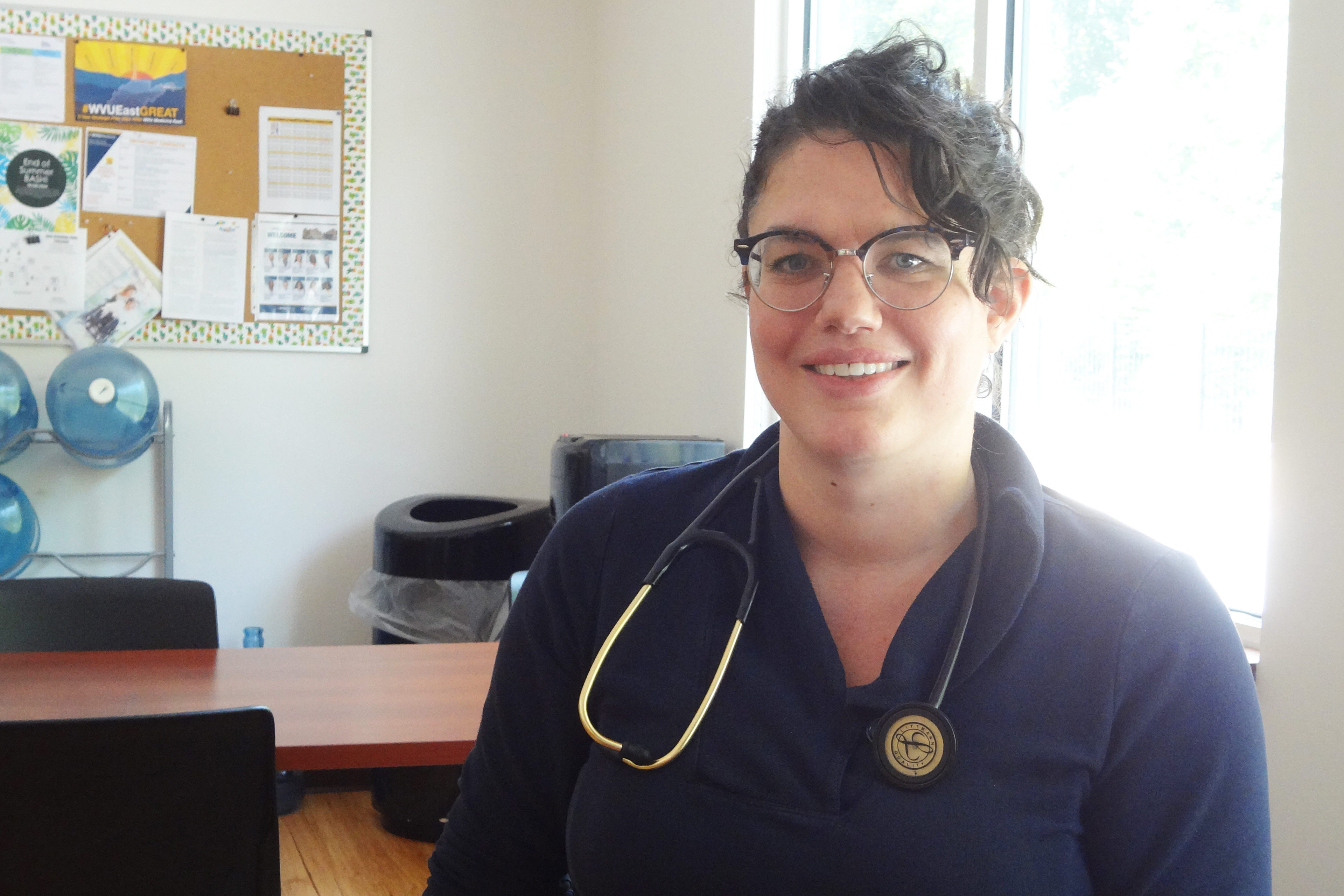 A portrait of Leila Elder, a woman with short brown hair and glasses. She has a stethoscope hanging from her neck.