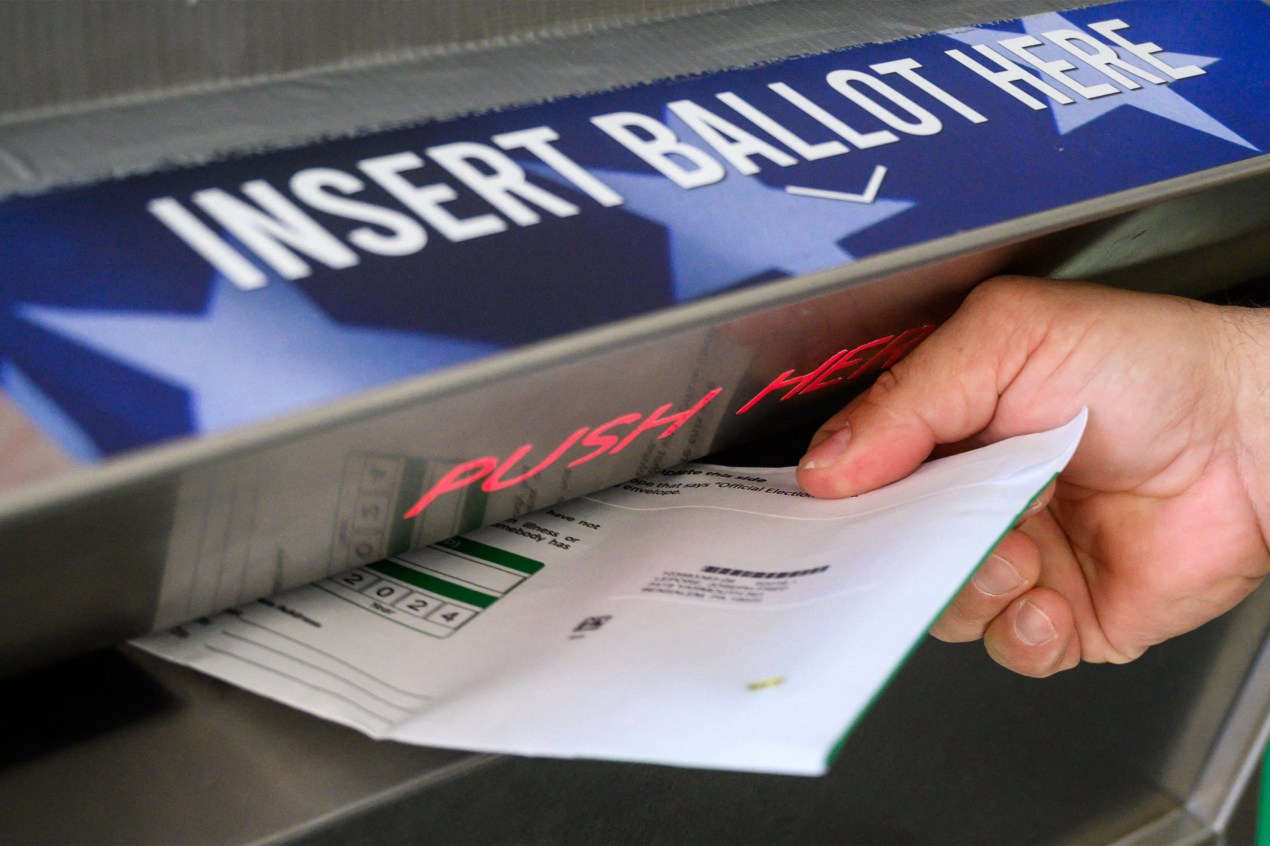 A photo of a person putting their ballot into a drop off box.