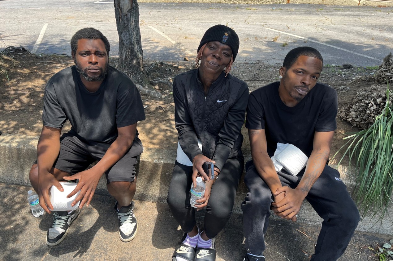 Three people sit on the curb looking up at the camera