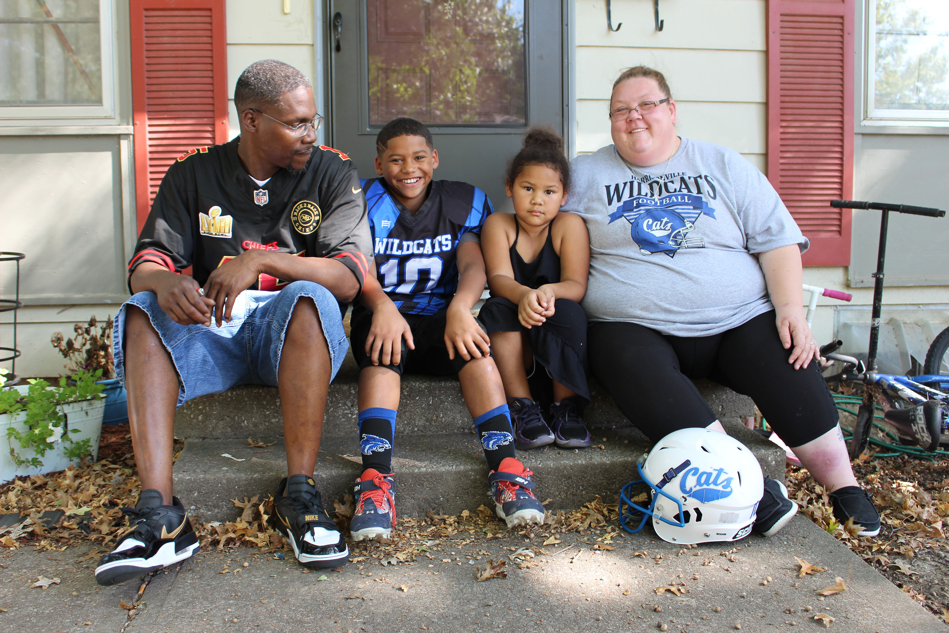 A man and a woman sit on the front step of a home, posing for a photo with two young children seated in between them